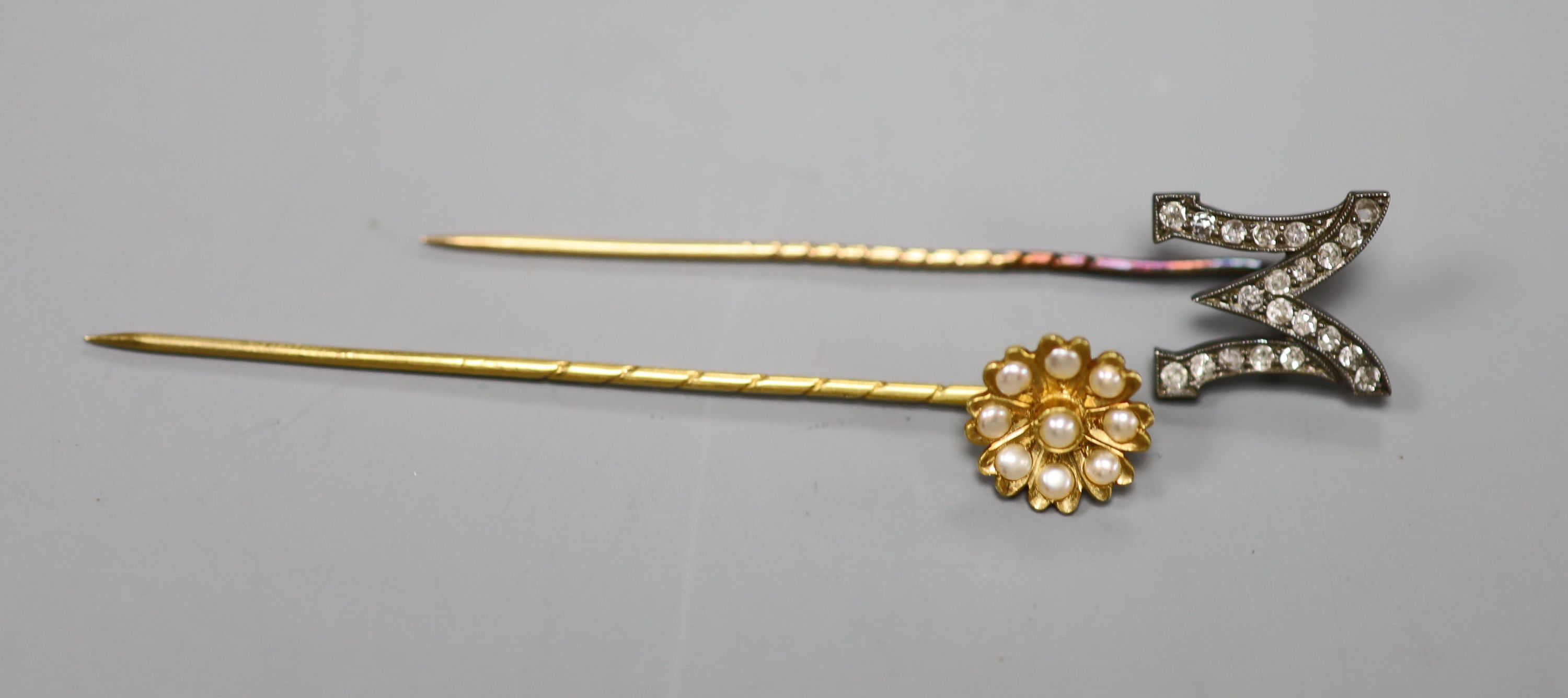 An early 20th century yellow metal and rose cut diamond set M stick pin, 58mm, gross 1.8 grams & 1 other stick pin.